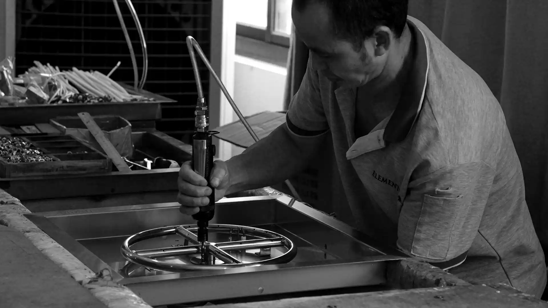 The controlled spray process in the Elementi workshop: fibre gun, mould, operator at work. Workshop light, no staged smiles.